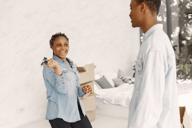 Mujer joven feliz sosteniendo llaves de su nuevo hogar, con cajas de mudanza